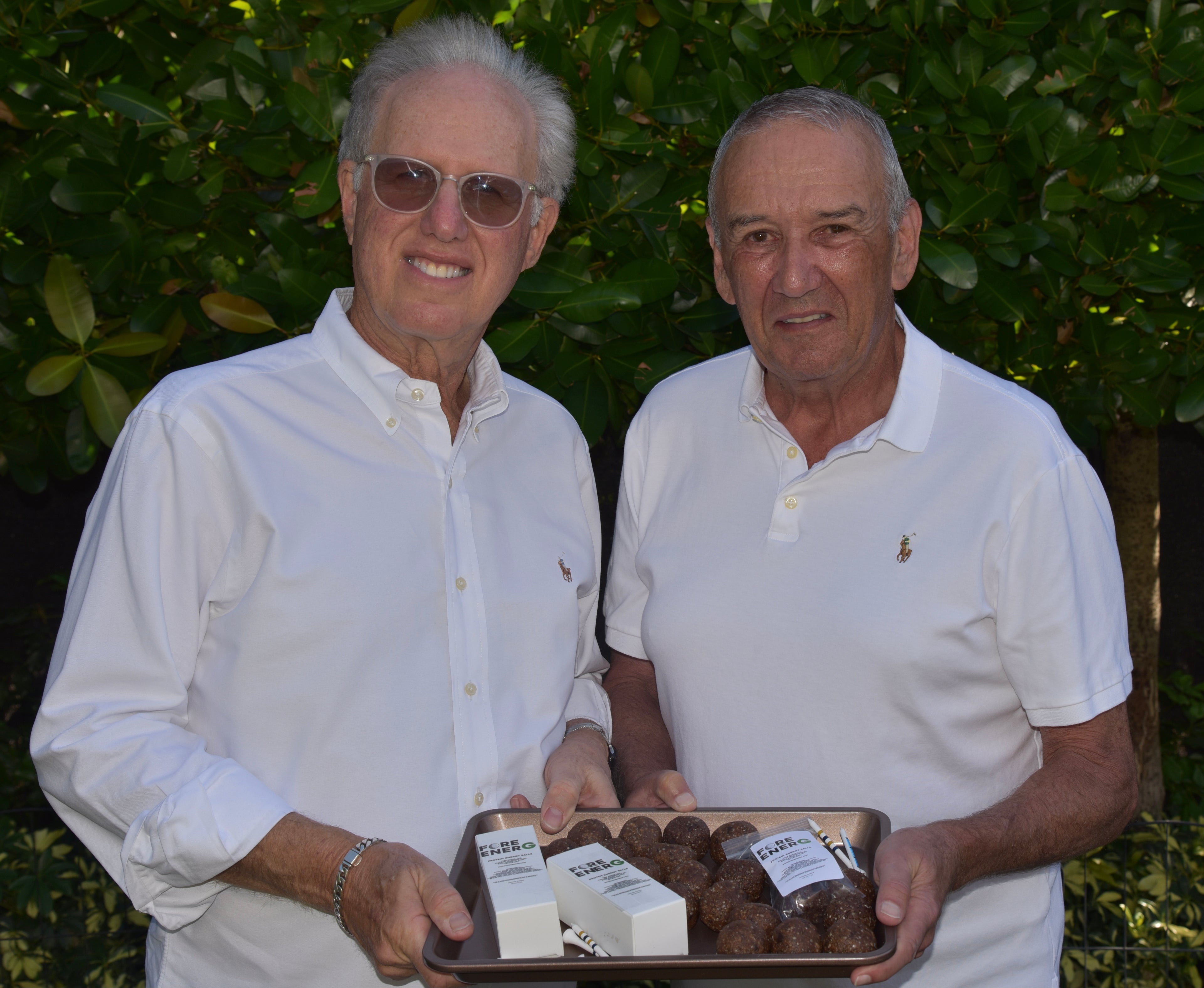 Two men holding a tray of Fore EnerG protein balls against a green leafy background